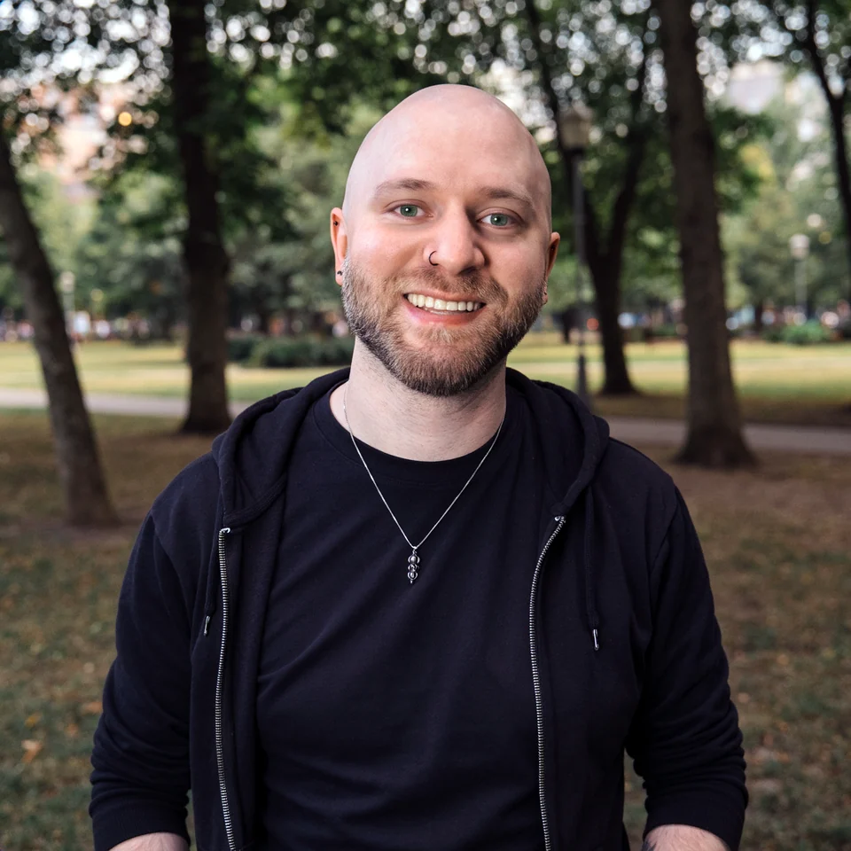 Joshua Meadows smiling in a park, wearing a black hoodie